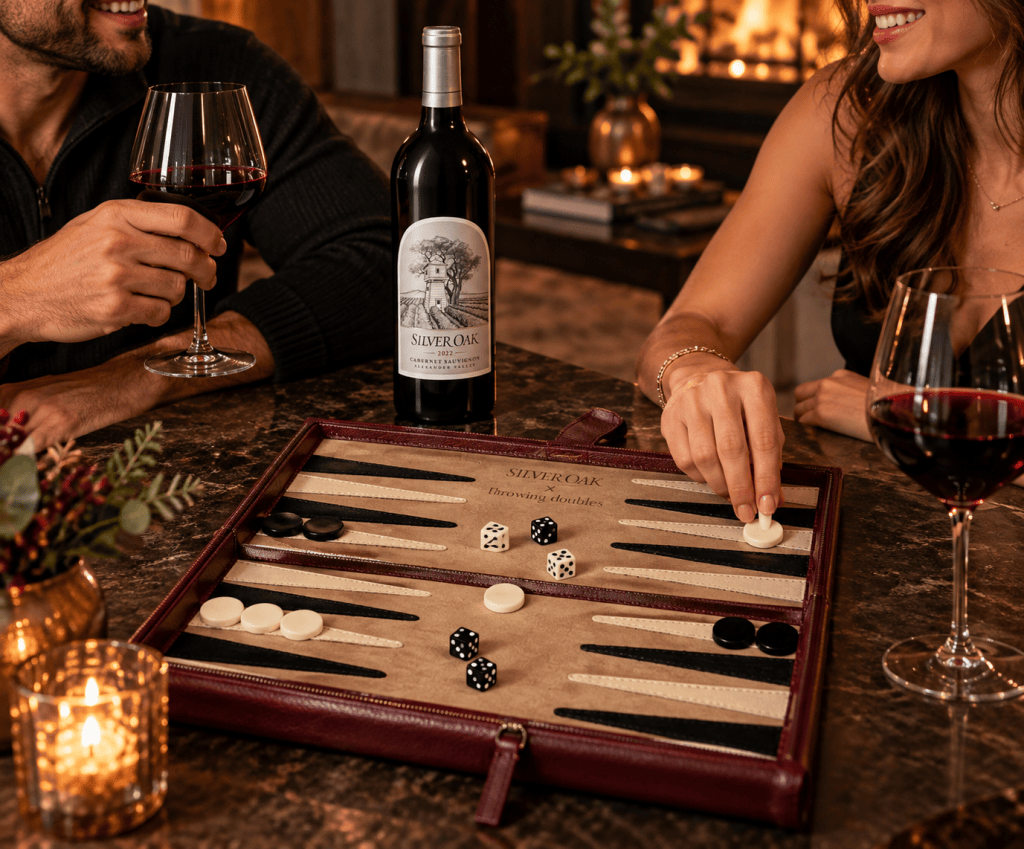 A cozy scene featuring a man and a woman enjoying a game of backgammon while sipping red wine. The table displays a backgammon board with black and white pieces, alongside two dice and a bottle of Silver Oak wine. Soft lighting creates an inviting atmosphere.