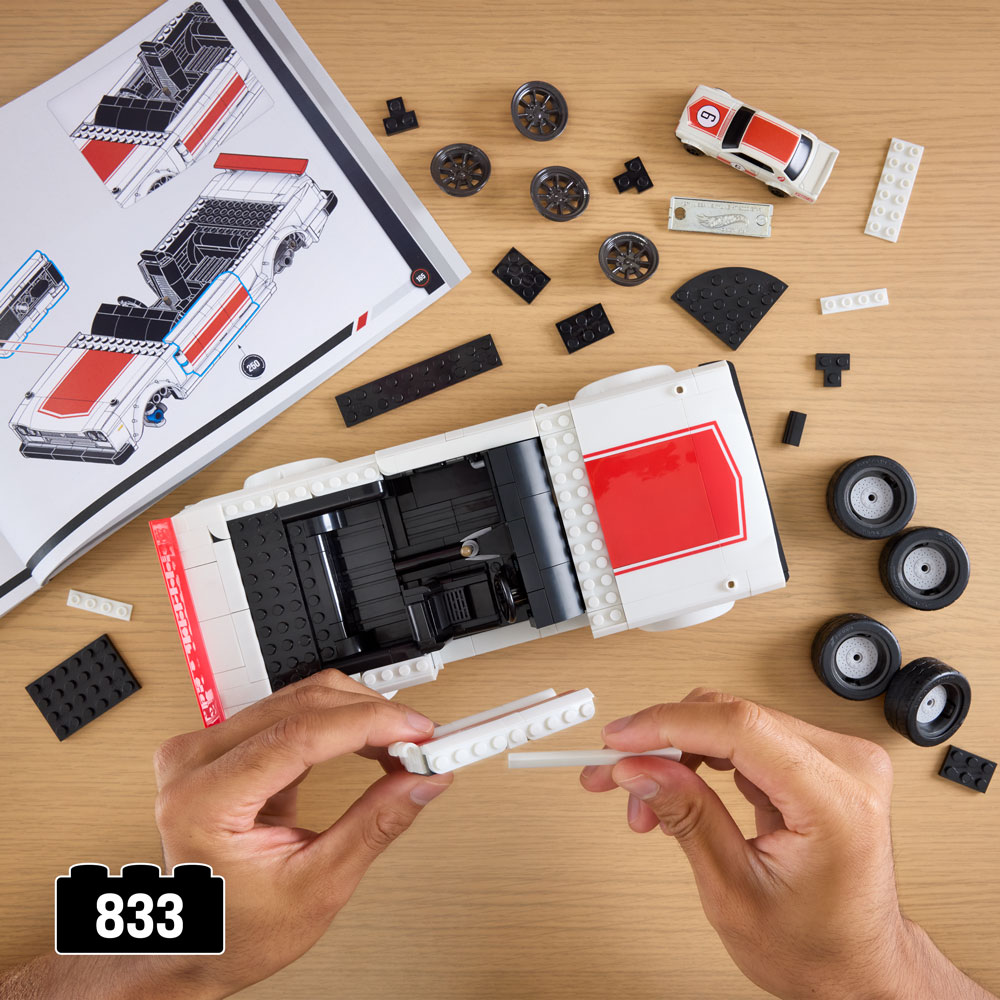 A top view of a building process for a toy vehicle set, featuring a white car with red accents. There are various LEGO pieces and wheels scattered around, along with a building manual.