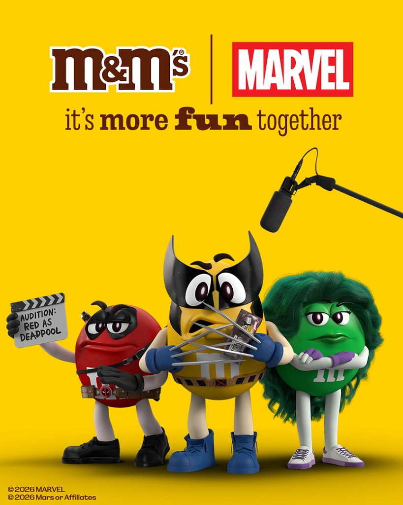 Three M&M's characters dressed as Marvel superheroes stand against a yellow background, promoting a collaboration between M&M's and Marvel. The red character holds a film slate, while the yellow character has claws, and the green character looks unimpressed.